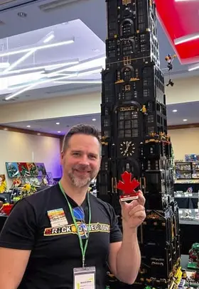 Shane Weckstrom, Lego builder and founder of Brick Connections, holding a Lego maple leaf beside a towering Lego build